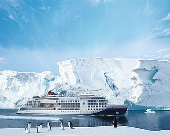Kreuzfahrtschiff vor einem Eisberg mit Pinguinen im Vordergrund